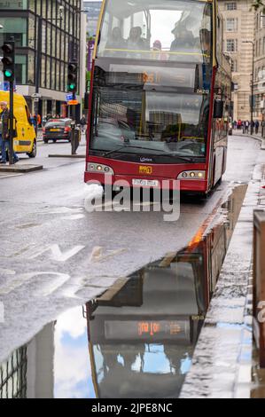 LONDON - May 20, 2022: Open top London Double Decker Tour Bus approaches large puddle with reflection Stock Photo