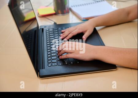 Close-up of the hands of a schoolchild typing text on laptop keyboard while studying in an online school. Homeschooling Stock Photo