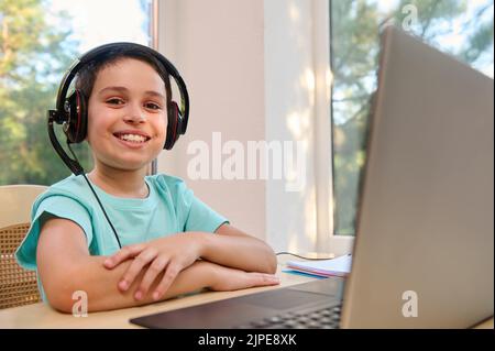 Adorable, smart student of an online school, in headphones, smiles at the camera, studying from anywhere in the world Stock Photo