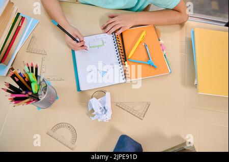 Top view of a schoolchild doing his homework on the geometry. Workbooks, pencil-case, school supplies lying on the table Stock Photo