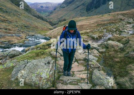 Female hiker walking up a mountain path towards Styhead Tarn in Borrowdale, Lake District National Park, Cumbria Stock Photo