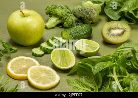 Chopped cucumber, kiwi and lime halves, an apple. Broccoli, basil sprigs and lettuce on the table. Close up. Top view. Green background Stock Photo