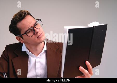 Lawyer reading a book confused. Business man in a brown suit, white shirt and glasses while he reads his notes. Thoughtful elegantly dressed man Stock Photo