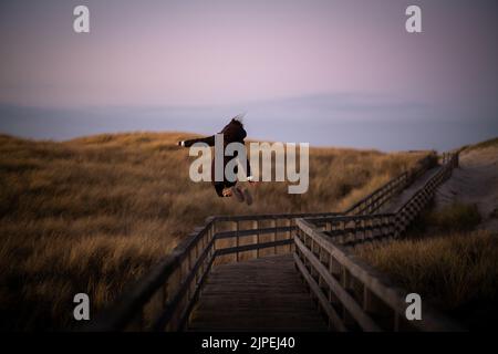Young woman jumps on boardwalk on Sylt, Germany Stock Photo