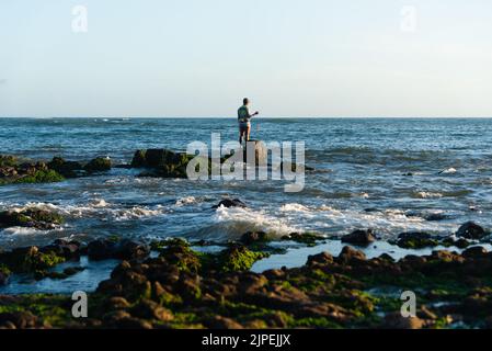 Salvador, Bahia, Brazil - December 11, 2021: Fisherman fishing from above the slippery rocks of Rio Vermelho beach in Salvador, Bahia. Stock Photo