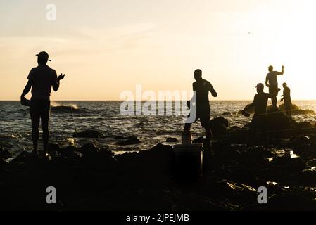 Salvador, Bahia, Brazil - December 11, 2021: Five fishermen fishing from above the rocks of Rio Vermelho beach in Salvador, Bahia. Stock Photo