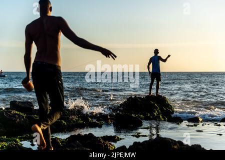 Salvador, Bahia, Brazil - December 11, 2021: Two fishermen fishing from above the rocks of Rio Vermelho beach in Salvador, Bahia. Stock Photo