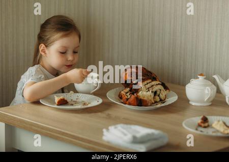 The girl eats a cake with a spoon and drinks tea. Close-up. Stock Photo