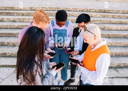 group of friends chatting and browsing with smartphones in a group. Stock Photo
