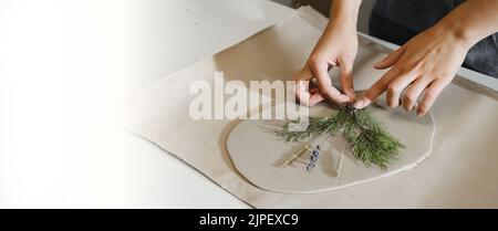 Banner Clay handmade Ceramic plates rolled on the table with plants and flowers. Top view on handcrafted pottery, close-up Stock Photo