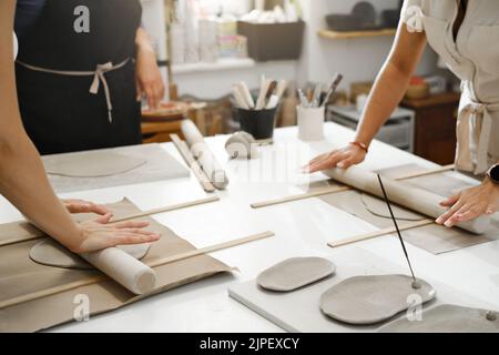 Pottery workshop in sunny studio. People working with clay on the table. Adults learning to do ceramic plates. Pottery as hobby and leisure activity Stock Photo