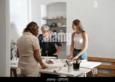 Pottery workshop in studio. People working with clay on the table. Adults learning to do ceramic plates. Pottery as hobby and leisure activity Stock Photo