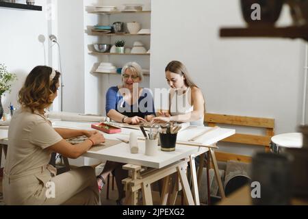 Pottery workshop in studio. People working with clay on the table. Adults learning to do ceramic plates. Pottery as hobby and leisure activity Stock Photo