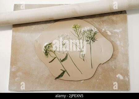 Clay handmade Ceramic plates, rolled clay on the table with plants and flowers. Top view on handcrafted pottery Stock Photo