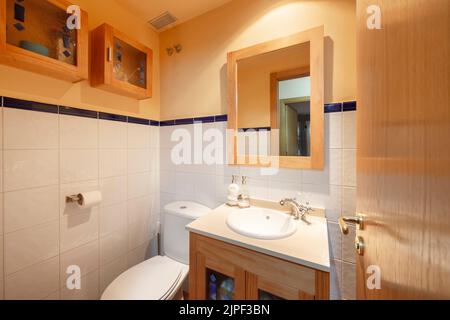White tile and orange paint bathroom with white porcelain sink, matching wood cabinets, wood framed mirror Stock Photo