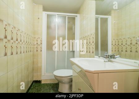 Simple bathroom with small vanity with white porcelain sink and frameless mirror, walk-in shower with glass partition and green flooring Stock Photo