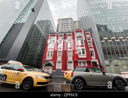 Moscow, Russia, August 2021: An old little red brick house stands between huge gray glass skyscrapers. Mix historical and modern, new and old. togethe Stock Photo