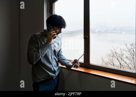 Latino businessman working in an office overlooking the river. Talking on the phone and reviewing notes Stock Photo