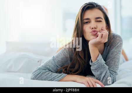 Shes a heartbreaker. Portrait of an attractive young woman blowing a kiss while lying in bed at home during the day. Stock Photo