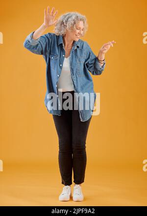 Fun, happy and cheerful woman dancing, celebrating and enjoying life alone against an orange background. Senior woman feeling excited, joyful and Stock Photo