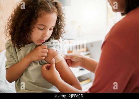 Covid nurse vaccinating child putting a bandage on at a clinic. Doctor applying plaster on girl after an injection at health centre. Pediatric Stock Photo