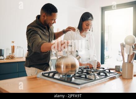 Loving couple having coffee or tea, relaxed and carefree while bonding in a kitchen at home. Caring husband being affectionate, talking and enjoying Stock Photo