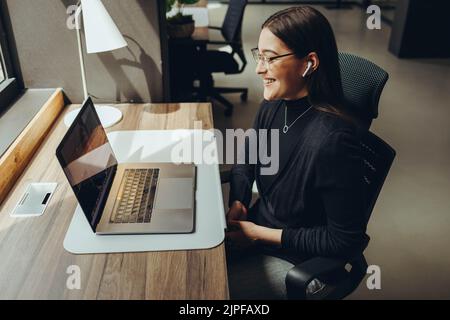 Happy young businesswoman smiling during a virtual meeting in a modern co-working office. Cheerful female entrepreneur communicating with her business Stock Photo