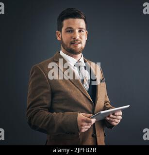 Ready for business now that Ive got my smart tools. Studio portrait of a handsome young businessman using a digital tablet against a dark background. Stock Photo