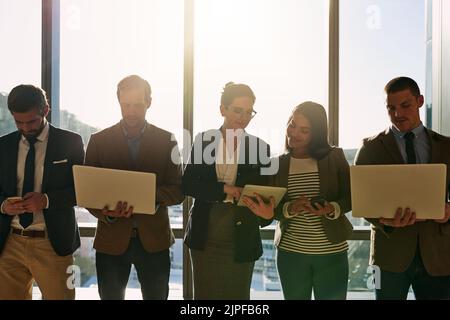 Wireless is the only way to work. a group of businesspeople using wireless devices while standing in the office. Stock Photo