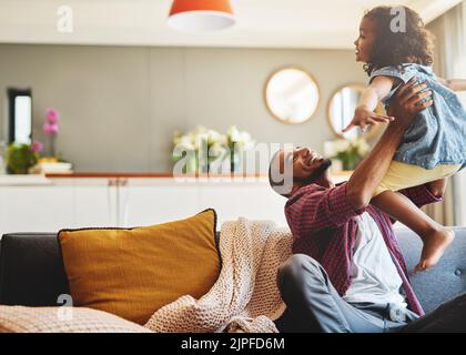 Im not coming back down daddy. an affectionate young father lifting his daughter playfully in their living room at home. Stock Photo