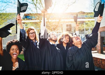 This is what we sacrificed sleep for. a group of students throwing their caps into the air after graduating. Stock Photo
