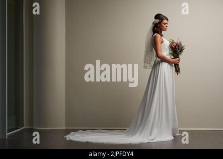 Stunning is the bride to be. Studio shot of a young beautiful bride posing against a grey background. Stock Photo