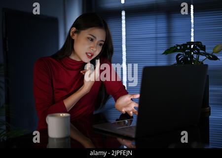 Beautiful and professional young Asian businesswoman or female office employee on the phone with her partner during working in the office till at nigh Stock Photo