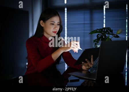 Professional and smart young Asian businesswoman or female manager  concentrating on a business project while using a tablet and working late at the o Stock Photo