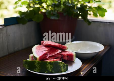 Sliced juicy red watermelon lies in a plate on the balcony. The concept of summer and delicious vegetables. Front view. Stock Photo