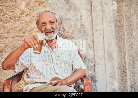 Have a seat and let me tell you a story. Portrait of a senior man drinking and smoking outside on the sidewalk of an ancient city. Stock Photo