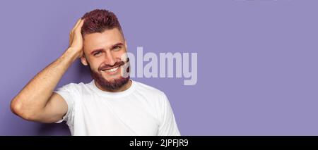 Portrait of handsome man with dyed hair and beard on violet background with space for text Stock Photo