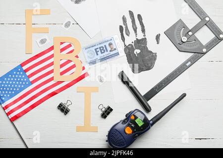 Abbreviation FBI with flag of USA, palm print, identification document of agent and portable radio transmitter on table Stock Photo