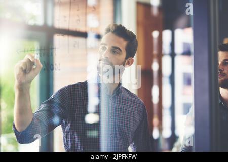 Theyve got a foolproof plan of action. two young businessmen brainstorming on a glass wall in an office. Stock Photo