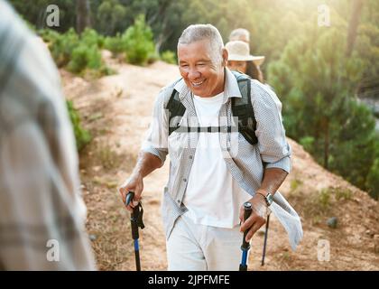 Hike, trekking sticks and senior male walking with friends for fitness and health in nature. Healthy, active and smiling mature man hiking with a Stock Photo