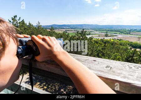 Boy child looking through binoculars on top of Hubertus lookout tower towards south, focus on mountains in background, Sopron, Hungary Stock Photo