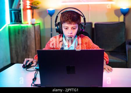 Teenager kid with headphones seriously playing online video game on laptop at home - concept of pro gamer, cyberspace and technology. Stock Photo