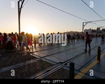 People walking along the Luis I bridge and admiring the view in Porto, Portugal. Tram or metro train lines can be seen on the bridge. Stock Photo