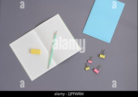 top view of open notebook with pencil, eraser, clips on grey background Stock Photo