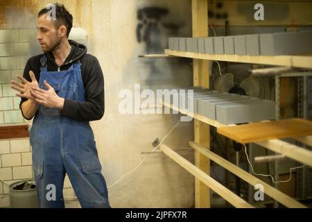 Guy with blue jumpsuit at work. Man in warehouse. Paint shop. Person works. Man rubs his hands. Stock Photo