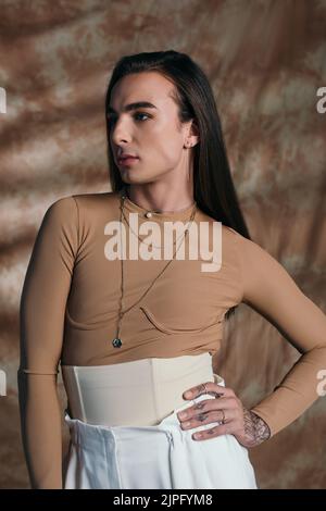 Queer person in corset posing and looking away on abstract brown background Stock Photo