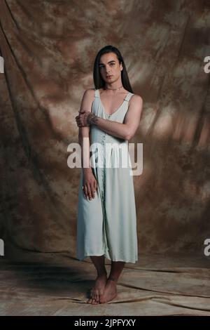 Full length of queer person in dress standing on abstract background Stock Photo