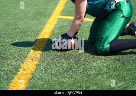 White female gloved hands reach for a Wilson American Football rolling on an fake grass pitch Stock Photo