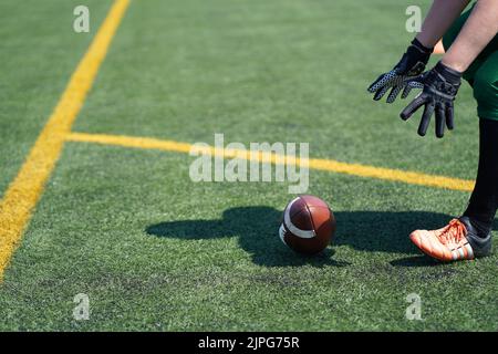 White female gloved hands reach for a Wilson American Football rolling on an fake grass pitch Stock Photo