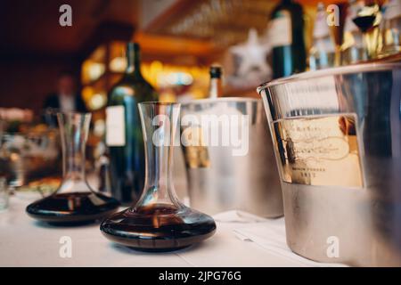 the waiter pours elite red wine into the decanter on the table in the restaurant. Stock Photo